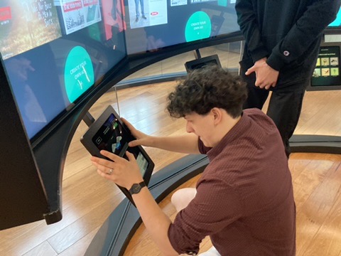 Ein junger Mann sitzt vor Monitoren und arbeitet an einem Touch Pad.