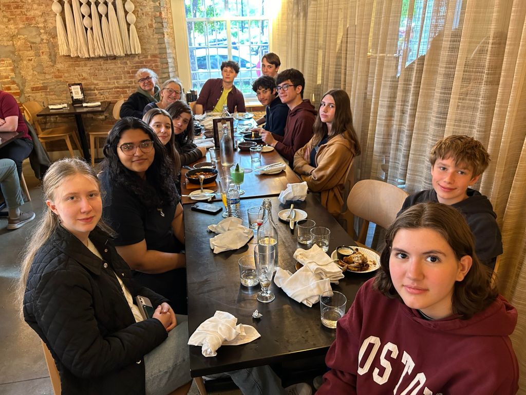 Eine Gruppe von Jugendlichen sitzt mit ihren beiden Lehrerinnen um drei zusammengestellte braune Tische in einem Restaurant